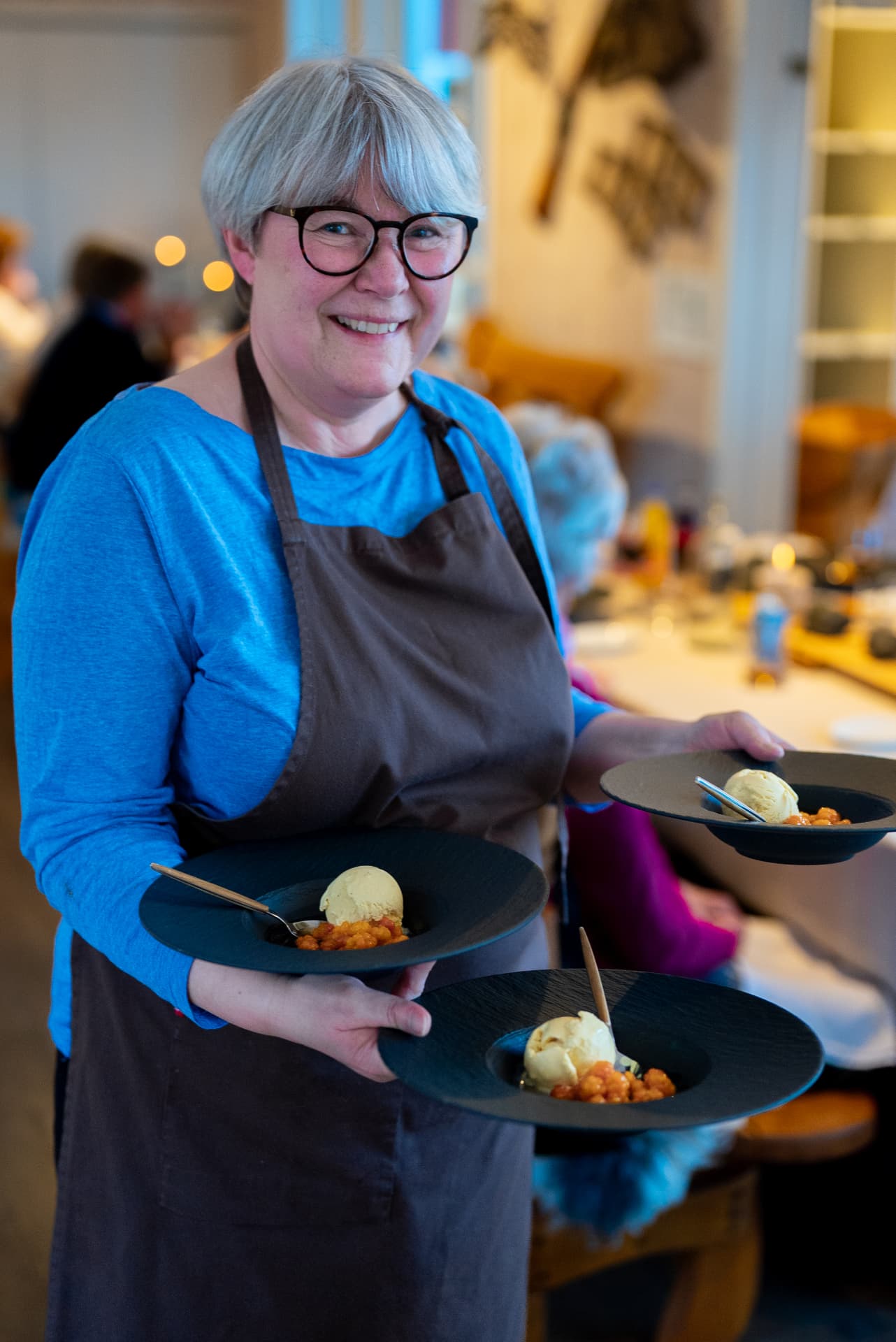 Vertskapet bærer fram dessert med multer til gjester ved langbordet på Livland Gård